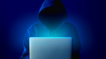 Portrait of anonymous man in black hoodie and mask hacking into computer or laptop. Scammer. Dark web. Cyber attask dafety.