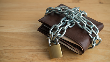 Leather wallet tied up steel chain and padlock on wooden table background. Money saving, shopaholic stop buying, money security protection, personal financial, risk management concept.